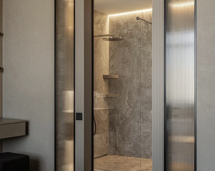 Фото сучасного інтер'єру з входом у душову кімнату. Дверний отвір обрамлений стінами з натурального сірого каменю. По обидва боки від дверей розташовані стаціонарні рифлені скляні панелі.