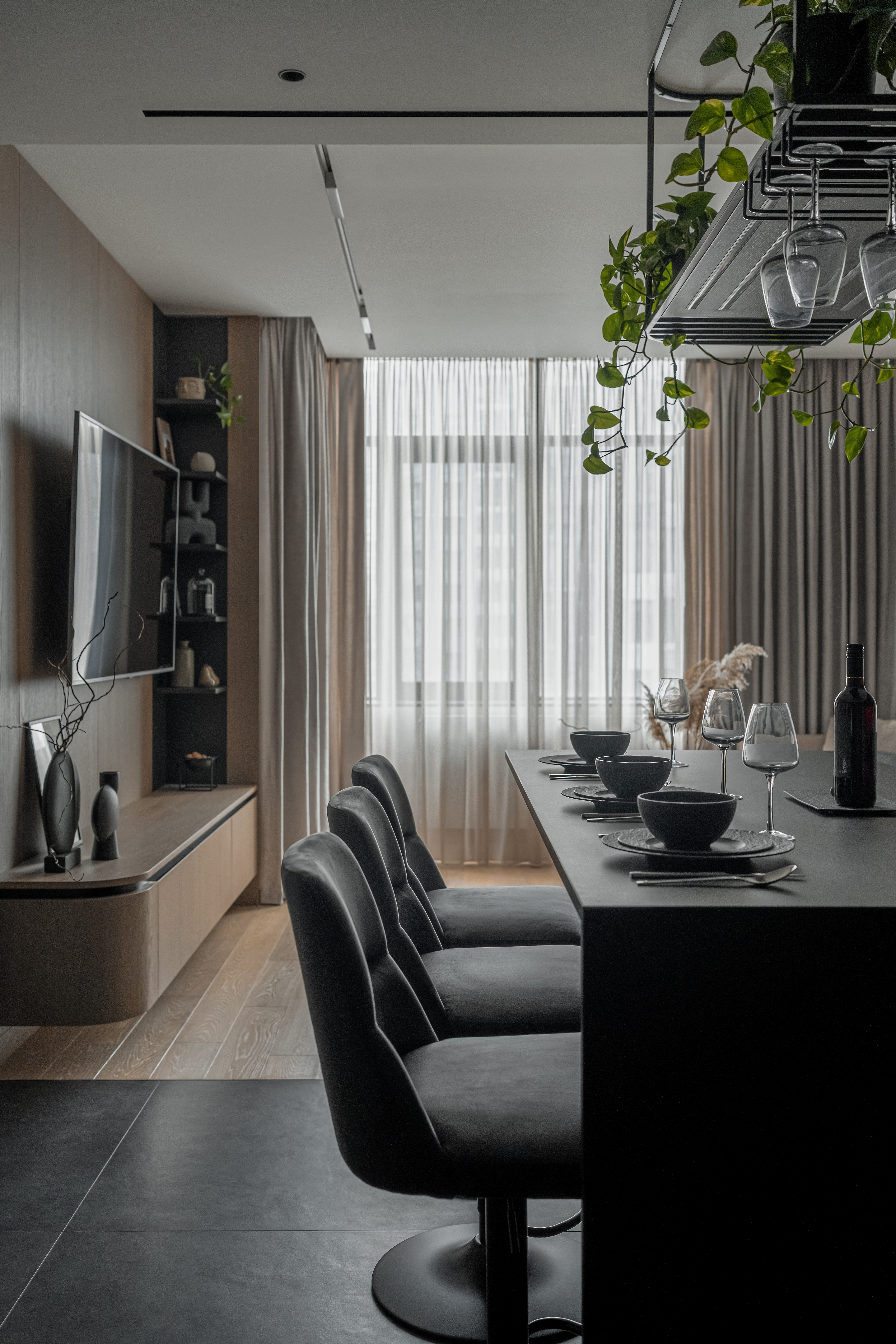 Сучасна кухня-їдальня з чорним кухонним островом, високими м’якими стільцями, підвісними келихами та панорамним вікном у фоні.